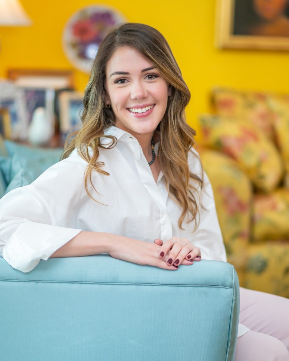 Laura Morales, fundadora de Nudge Labs, sonriendo en un sofá turquesa frente a una pared amarilla